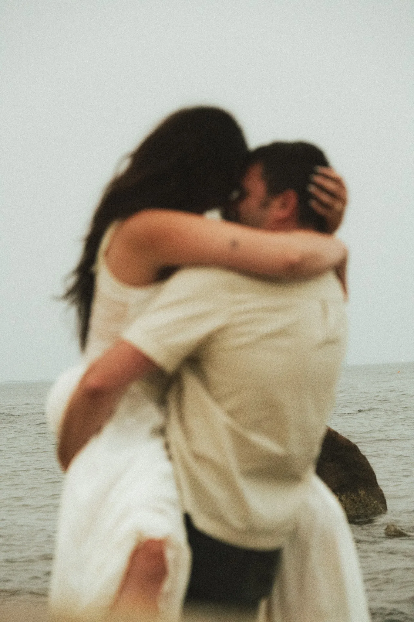 A bride and groom holding each other close, the water behind them.